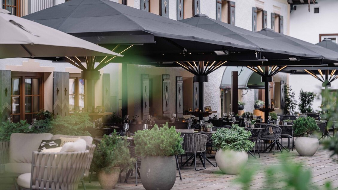 Eine elegante Terrasse mit großen Sonnenschirmen und stilvollen Möbeln. Grüne Pflanzen fügen eine natürliche Note hinzu. | © JOHANN Schladming