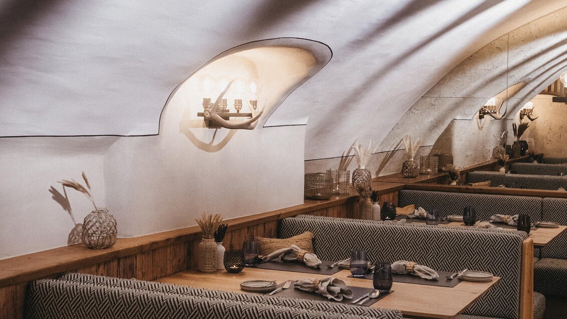 Ein stilvolles Restaurant mit gemütlichen Sitzbereichen und warmem Licht. Die Wände sind geschwungen und die Tischdekoration ist modern. | © JOHANN Schladming