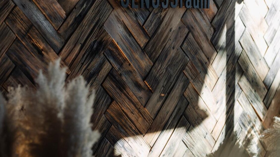 Eine stilvolle Wand aus Holz mit einem modernen Schriftzug. Im Vordergrund sind dekorative Pflanzen zu sehen, die das Ambiente ergänzen. | © JOHANN Schladming