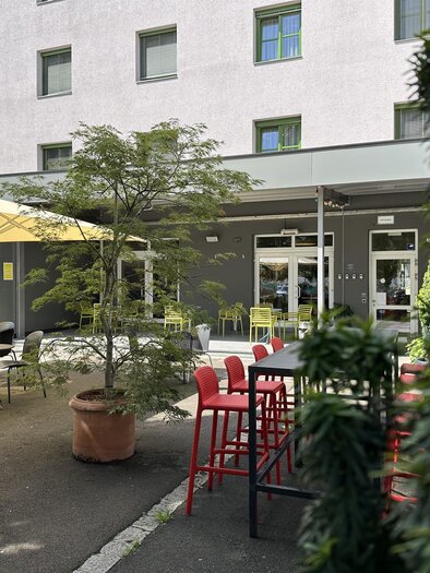 Ein einladender Außenbereich mit Tischen und Stühlen unter Sonnenschirmen. Pflanzen sorgen für eine grüne Atmosphäre. | © JUFA Hotels