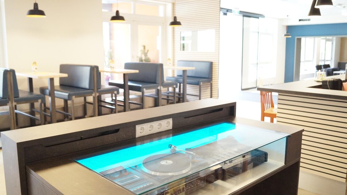 Moderner Sitzbereich mit Holztischen, Musiktheke und Retro-Plattenspieler. | © JUFA Hotels