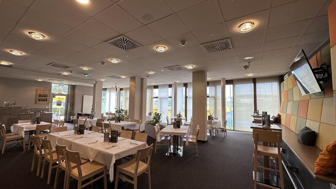 Ein modernes Restaurant mit Tischen und Stühlen. Der Raum ist hell erleuchtet und hat große Fenster, die einen Blick nach außen bieten. | © JUFA Hotels