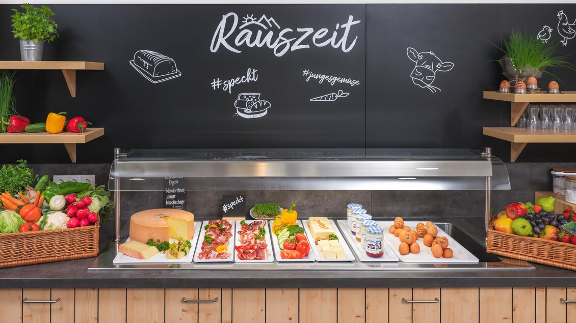 Ein Buffet mit frischen Lebensmitteln, darunter Gemüse, Käse und Snacks. Im Hintergrund steht die Schrift "Räuzzeit" an einer Wand. | © Lipizzanerheimat-JUFA
