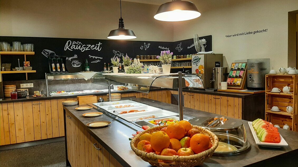 Ein einladender Frühstücksbereich mit einem großen Obstkorb und verschiedenen Speisen. Im Hintergrund sind Regale mit weiteren Angeboten sichtbar. | © Lipizzanerheimat-Lorenzoni