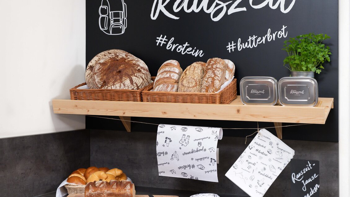 Ein rustikaler Küchenbereich mit verschiedenen Brotsorten und frischen Kräutern. An der Wand steht "Rauszeit" mit entsprechenden Hashtags. | © Lipizzanerheimat-JUFA