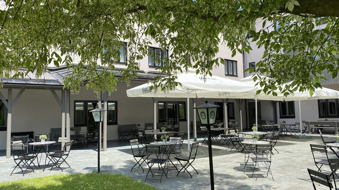 Eine einladende Terrasse mit Tischen und Stühlen unter einem schattenspendenden Baum. Im Hintergrund ist ein Gebäude zu sehen. | © Lipizzanerheimat-IQ Foto