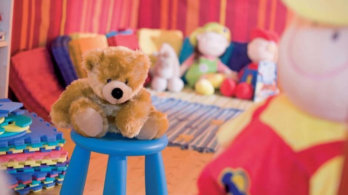Ein gemütlicher Spielbereich mit bunten Kissen und vielen Spielzeugen. Ein Plüschbär sitzt auf einem blauen Hocker. | © JUFA