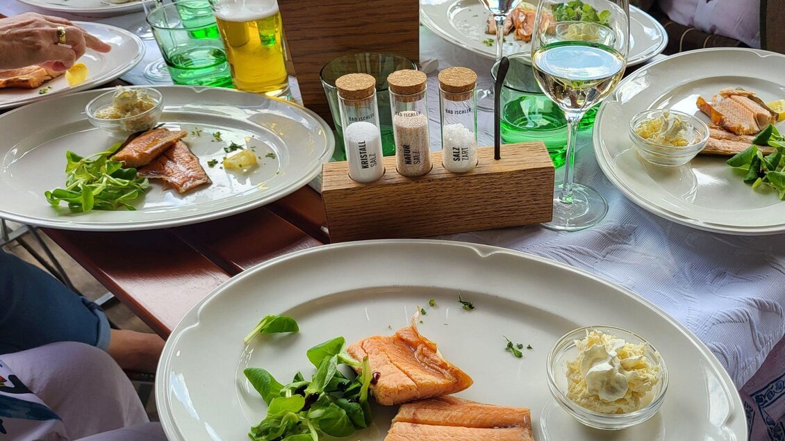 Eine stilvolle Tafel mit mehreren Tellern, die geräucherten Fisch und frischen Salat enthalten. Gläser mit Wasser und Wein sowie Gewürzbehälter ergänzen das gehobene Ambiente. | © Petra Kirchschlager