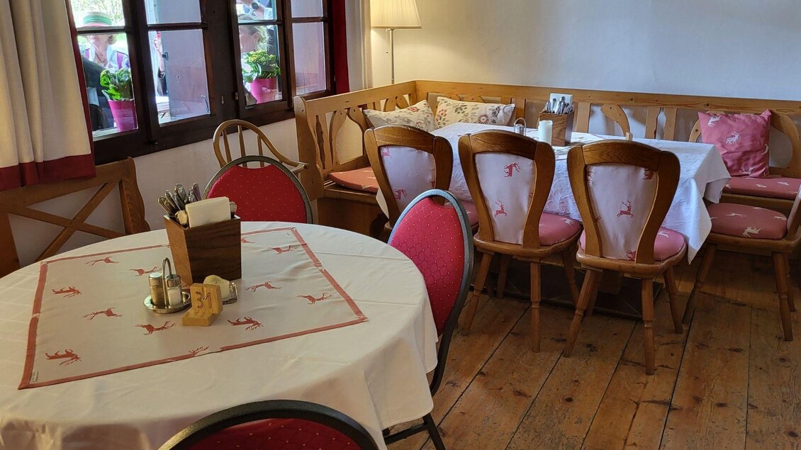 Ein gemütlicher Essbereich mit einem runden Tisch und roten Stühlen. Die Wände sind mit Fenstern und einem Holzregal dekoriert. | © Petra Kirchschlager