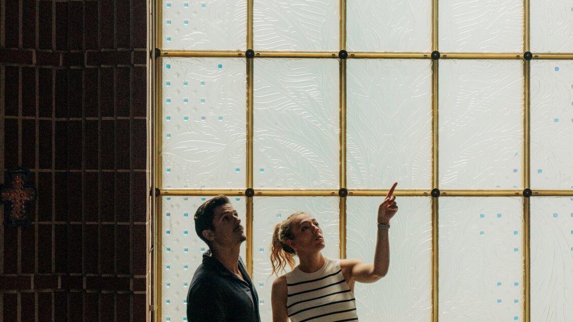 Zwei Personen stehen in einem Raum und betrachten ein großes Fenster. Eine Person zeigt auf etwas und beide scheinen interessiert zu sein. | © (c) Region Graz - studio draussen