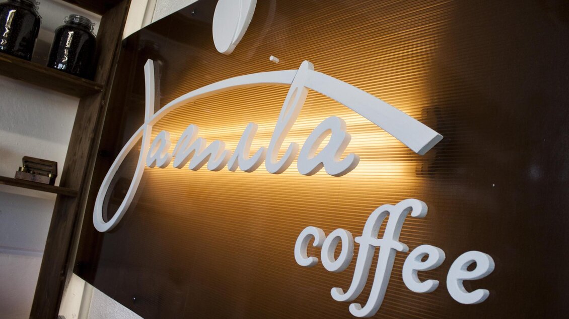 Ein elegantes Schild mit dem Schriftzug "Jambila Coffee". Der Hintergrund ist in warmen Farben gehalten. | © Jamila Coffee GmbH