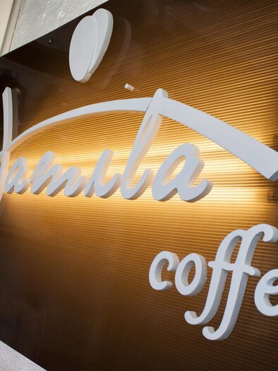Ein elegantes Schild mit dem Schriftzug "Jambila Coffee". Der Hintergrund ist in warmen Farben gehalten. | © Jamila Coffee GmbH