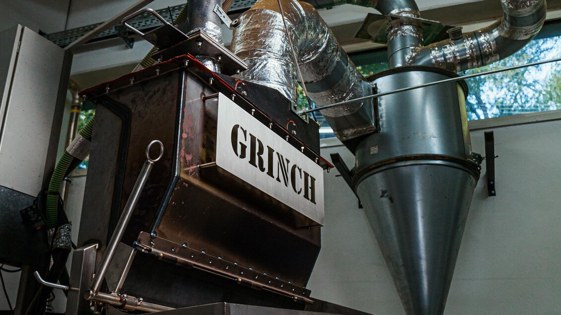 Eine Kaffeemaschine mit dem Namen "GRINCH" in einer modernen Rösterei. Rohre führen zu verschiedenen Bereichen der Maschine. | © Jamila Coffee GmbH