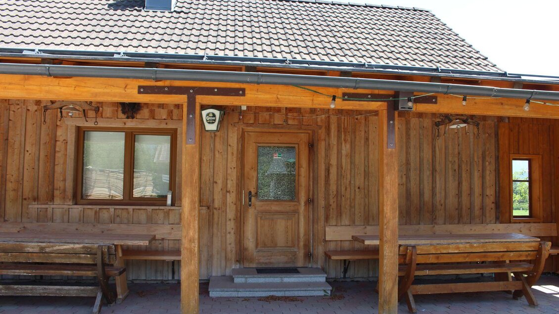 Ein traditionelles Holzhaus mit einem massiven Dach. Vor dem Haus befinden sich Holzbänke und Tische. | © Kogler`s Jausenhütt`n