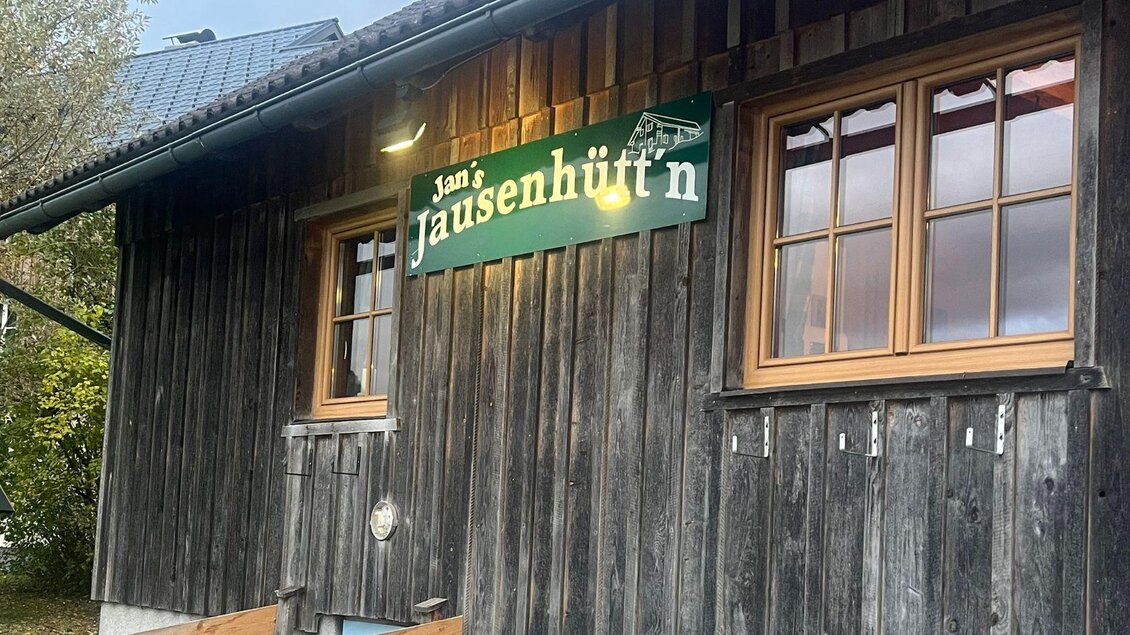 Ein rustikales Holzhaus mit einem Schild, das "Jan's Jausenhütn" zeigt. Die Fenster sind braun und die Fassade hat eine traditionelle Bauweise. | © TVB Ausseerland-Salzkammergut_Nathalie Schröttenhamer