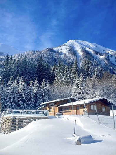 Eine malerische Winterlandschaft mit schneebedeckten Bergen und Tannenbäumen. Ein gemütliches Holzhaus liegt eingebettet im frischen Schnee. | © Marschnig