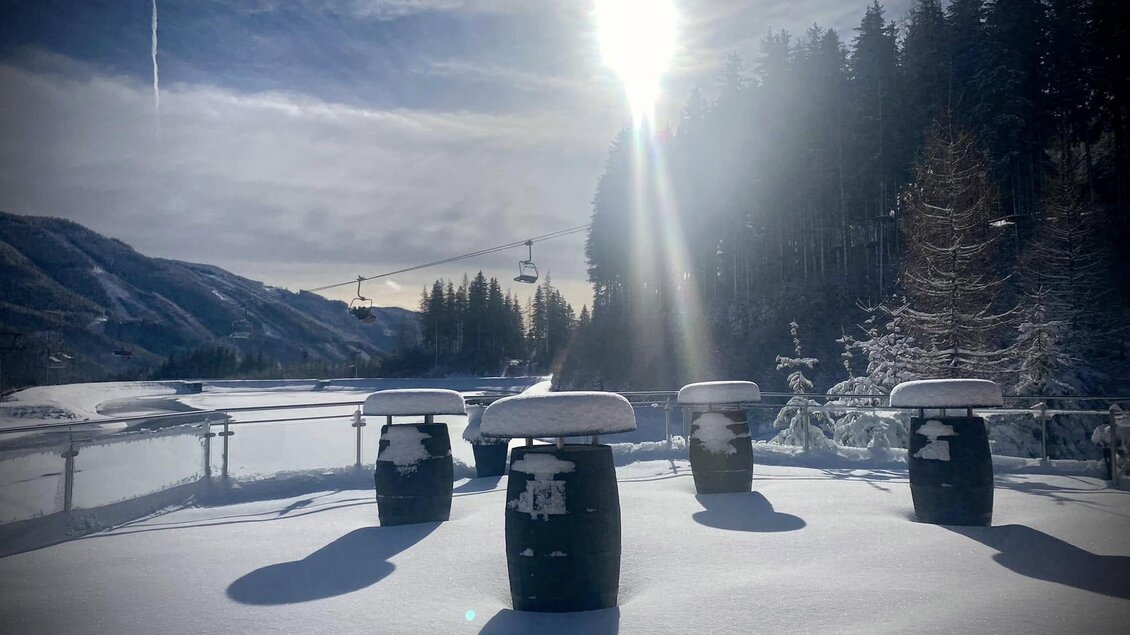 Eine verschneite Landschaft mit mehreren Fässern im Vordergrund. Im Hintergrund sind Bäume und Berge sowie ein strahlender Sonnenuntergang zu sehen. | © Marschnig