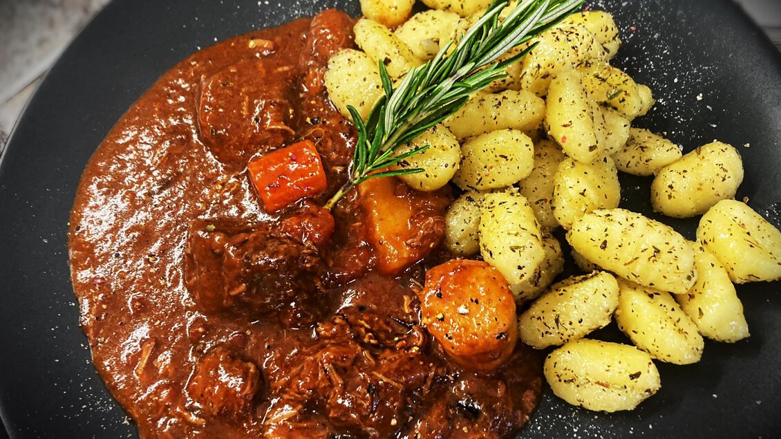 Ein herzhaftes Gericht mit zartem Rindfleisch in einer braunen Soße, serviert mit Gnocchi und frischen Kräutern. Die Platte ist ansprechend angerichtet und ideal für ein gemütliches Abendessen. | © Marschnig