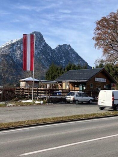 A building with an Austrian flag near a road, surrounded by mountains and trees. The scene depicts a tranquil, rural atmosphere. | © TVB_Ausseerland Salzkammergut_Heike Temmel