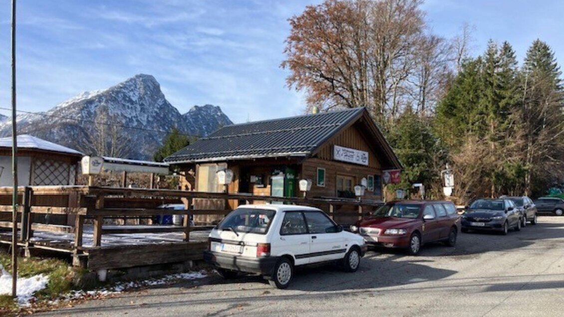 Ein kleines Holzhaus am Straßenrand, umgeben von Bäumen und Bergen. Mehrere Autos parken vor dem Gebäude. | © TVB_Ausseerland Salzkammergut_Heike Temmel