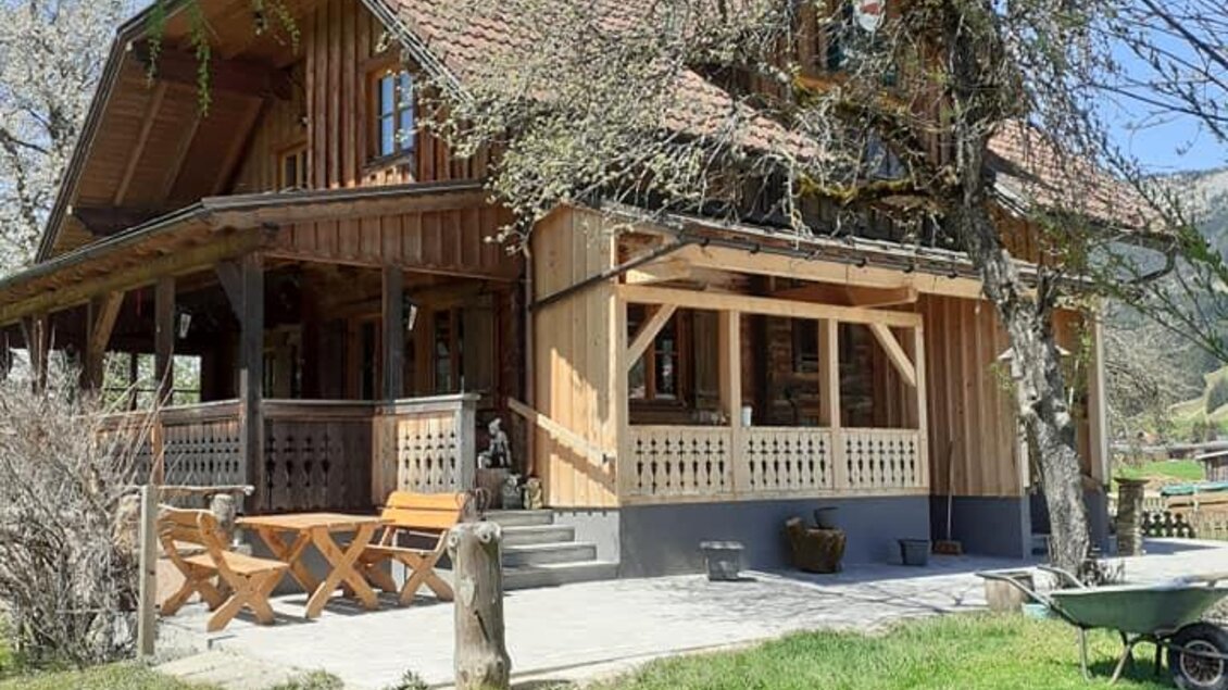 Ein charmantes Holzhaus mit einem großen Balkon. Der Garten ist grün und einladend, umgeben von Bäumen.