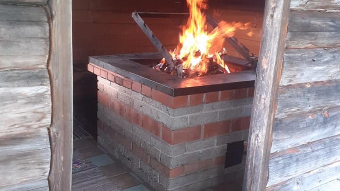 Ein offener Kamin in einer rustikalen Hütte. Flammen lodern aus dem Feuer, das für gemütliche Wärme sorgt.