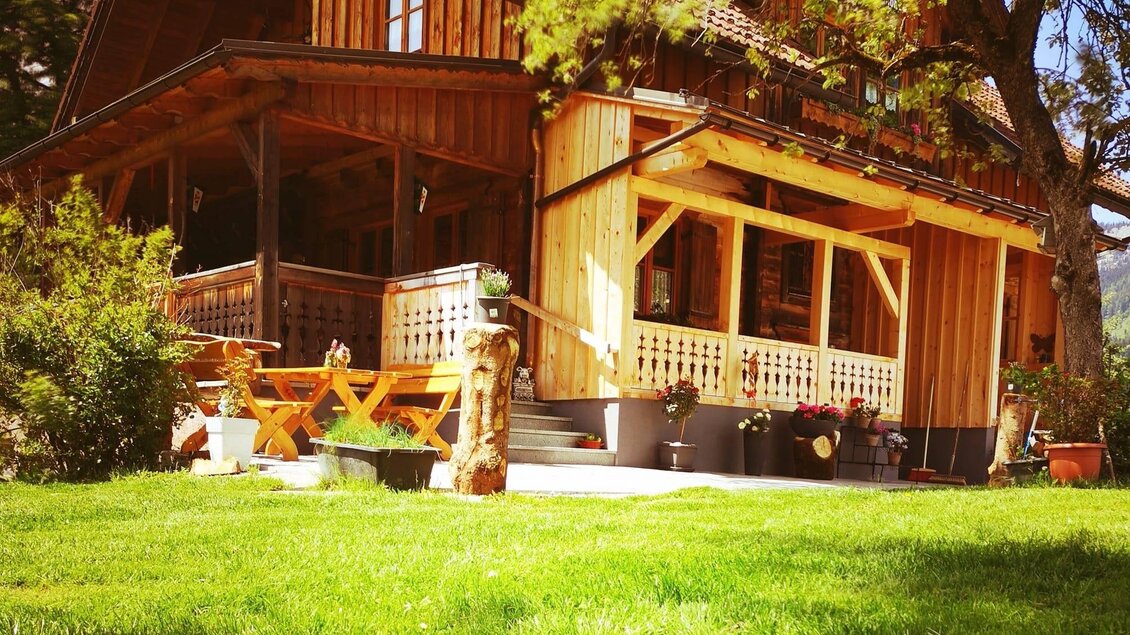 Ein charmantes Holzhaus mit einer großen Veranda und einem einladenden Garten. Umgeben von Bäumen und grüner Wiese ist es ein perfekter Ort zum Entspannen.
