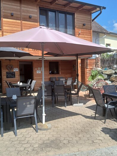 A cozy outdoor area with tables and chairs under sun umbrellas. In the background, a wooden building is visible. | © Sarah Windisch