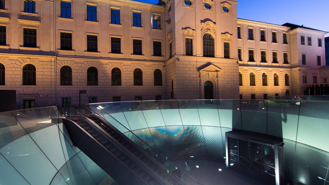 Blick auf den beleuchteten Eingang des Joanneumsviertels Graz in der Abenddämmerung | © Graz Tourismus-Harry Schiffer