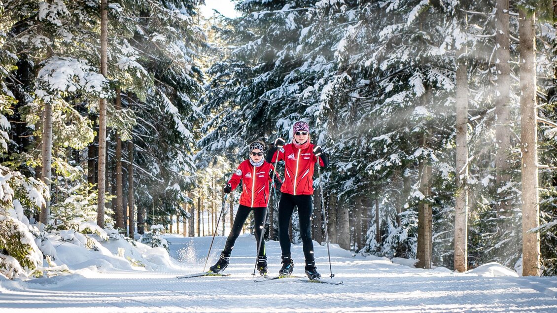 Zwei Skifahrer in roten Jacken genießen die Winterlandschaft. Umgeben von schneebedeckten Bäumen und einer klaren, sonnigen Atmosphäre. | © Oststeiermark Tourismus