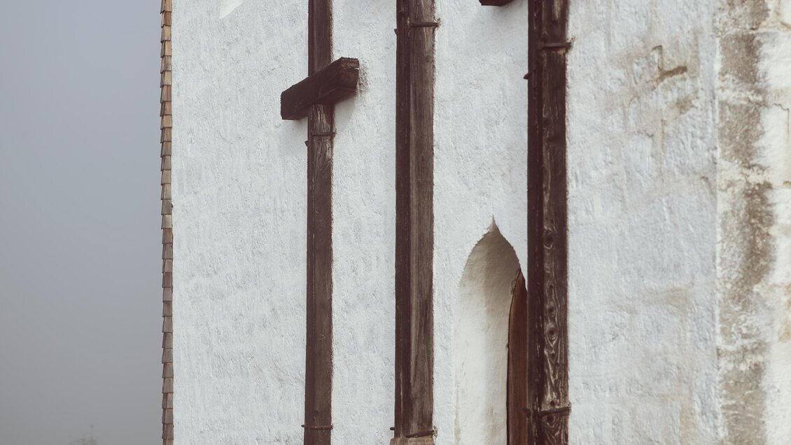 Eine alte Kirche mit drei großen Holzkreuzen an der Wand. Im Hintergrund ist dichter Nebel sichtbar. | © Armin Walcher