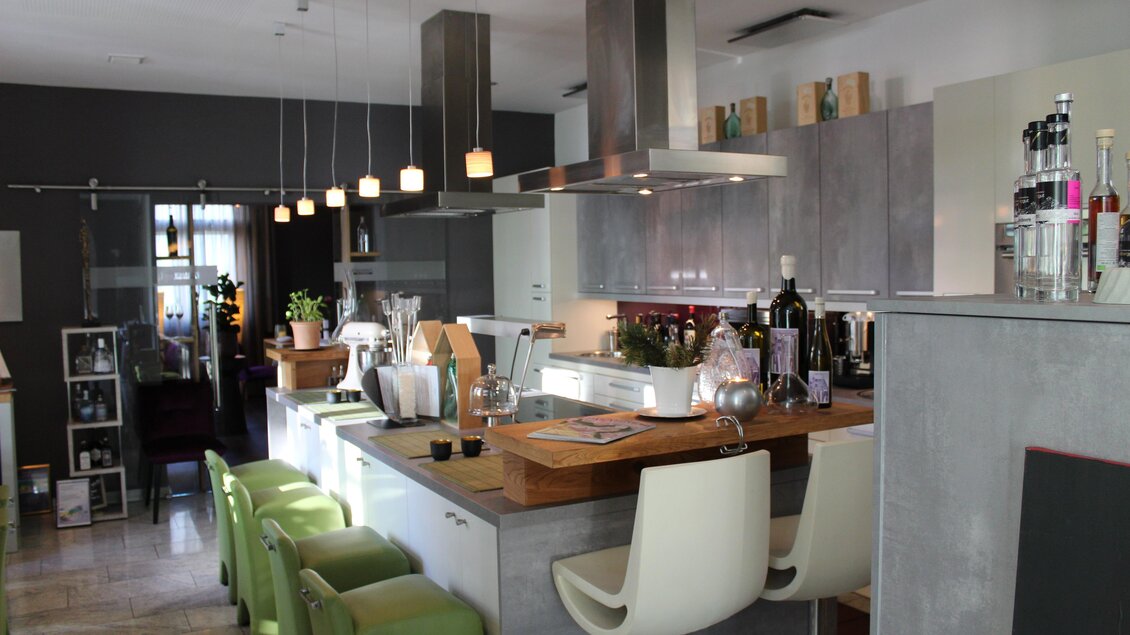 Eine moderne Küche mit einer Holzinsel und hängenden Lampen. Grüne Barhocker und verschiedene Pflanzen sorgen für eine einladende Atmosphäre. | © Co:/mikejohann