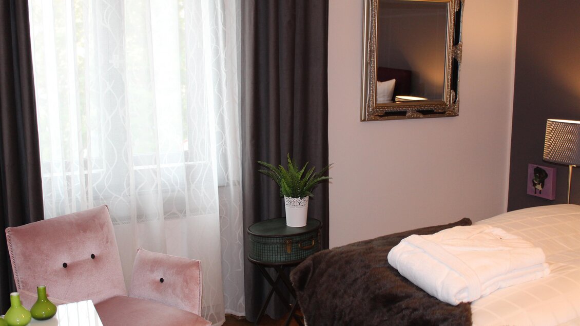 Ein gemütliches Schlafzimmer mit einem großen Fenster und weichen Vorhängen. Ein Beistelltisch und ein Pflanzenbehälter ergänzen die Einrichtung. | © Co:/mikejohann