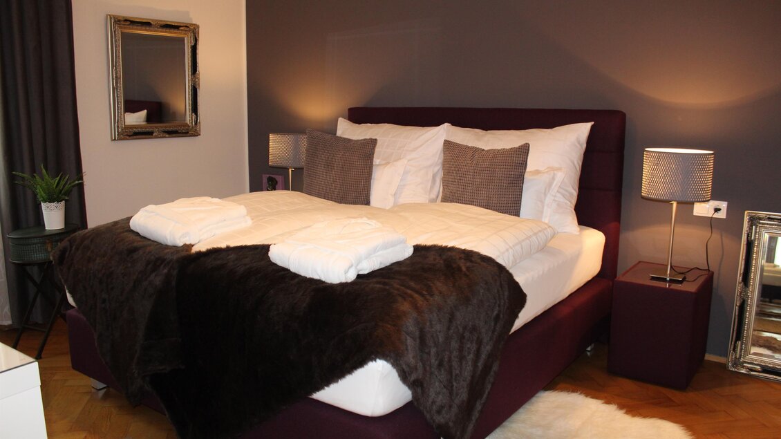 Ein gemütliches Schlafzimmer mit einem großen Bett, zwei Kissen und einer warmen Decke. Das Zimmer hat eine moderne Einrichtung und sanfte Beleuchtung. | © Co:/mikejohann