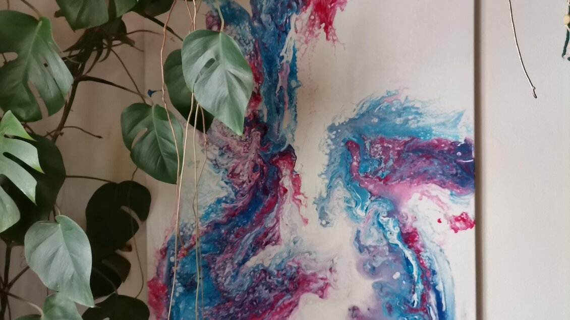 Ein abstraktes Gemälde mit lebendigen Farben in Blau, Pink und Weiß hängt an der Wand. Um das Bild herum wachsen grüne Pflanzen. | © Julia Hauck