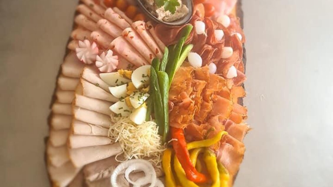 Eine große Wurst- und Käseplatte, kunstvoll auf einem Holzbrett angerichtet. Sie zeigt verschiedene Fleischsorten, Gemüse und garnierte Elemente. | © Köll Fleischfachgeschäft &amp; Catering