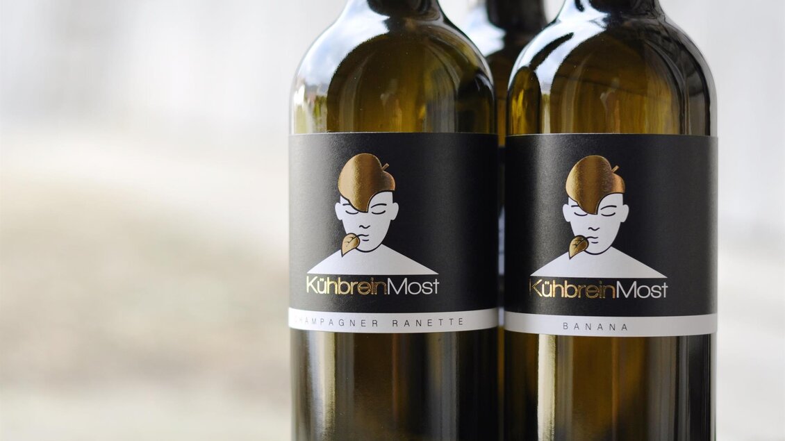 Zwei Flaschen Wein mit eleganten Etiketten stehen nebeneinander. Die Etiketten zeigen ein künstlerisches Design mit der Aufschrift "KühlbreinMost". | ©  Kühbrein