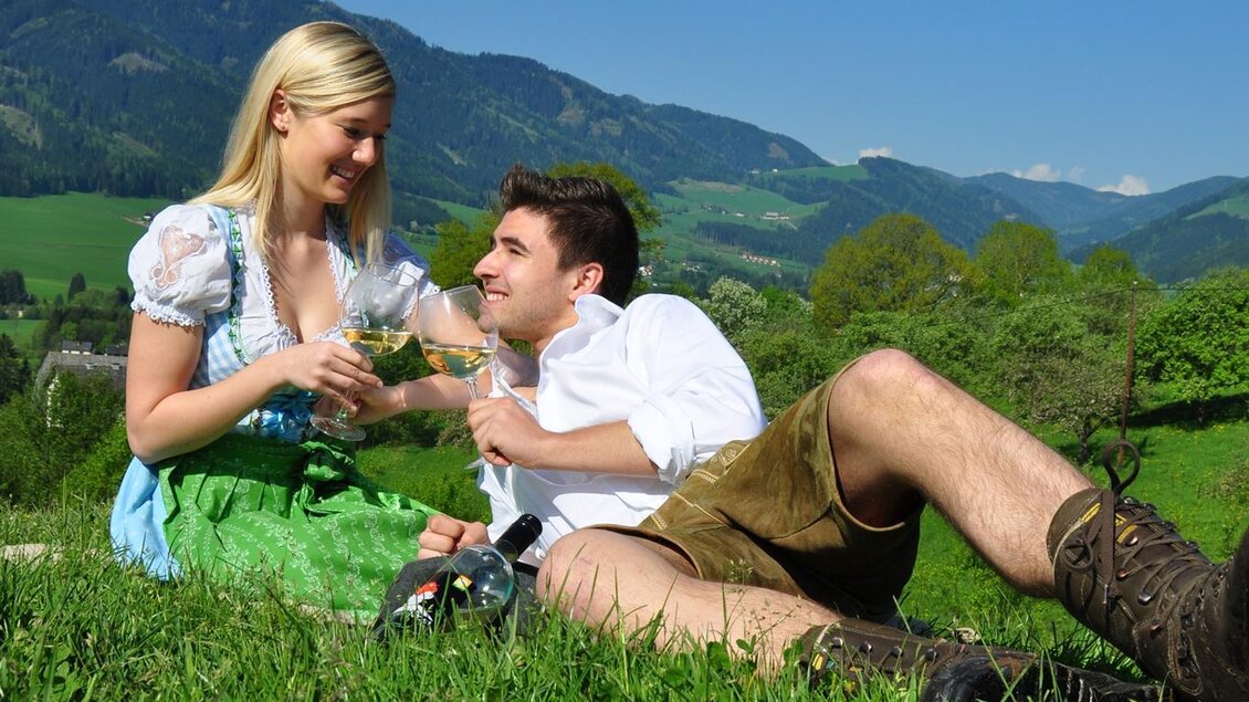 Ein Paar sitzt auf einer Wiese in den Alpen. Sie genießen die Natur und die sonnige Atmosphäre. | ©  Kühbrein