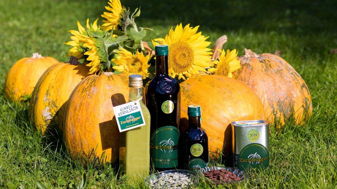 Eine Ansammlung von Kürbissen und Sonnenblumen in der Natur. Daneben stehen Flaschen mit Öl und anderen Produkten, die die Ernte repräsentieren. | © Region Graz -  Harry Schiffer
