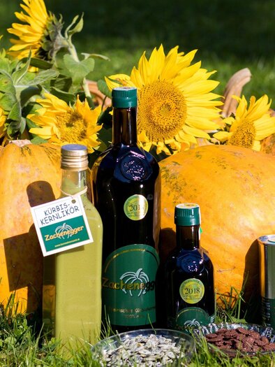 Eine Ansammlung von Kürbissen und Sonnenblumen in der Natur. Daneben stehen Flaschen mit Öl und anderen Produkten, die die Ernte repräsentieren. | © Region Graz -  Harry Schiffer