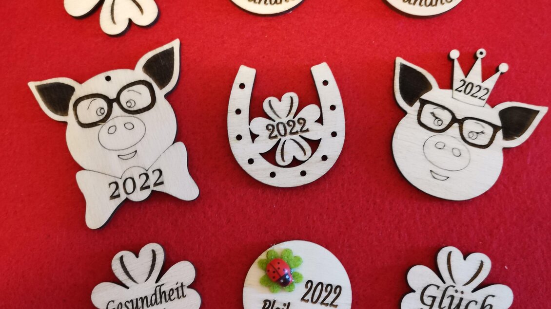 Eine Sammlung von Glücksbringern und Motiven für das Jahr 2022. Die Designs umfassen Schweine, Blumen und andere Symbole für Gesundheit und Glück. | © KM Lasergravuren