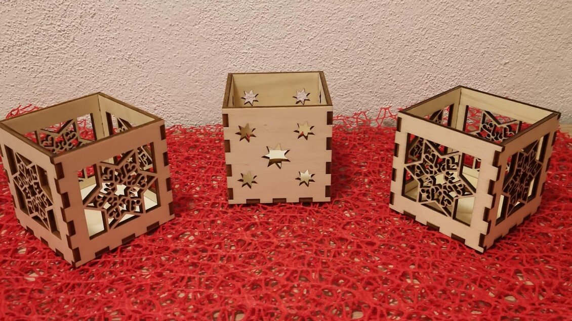 Drei dekorative Holzbehälter stehen auf einem roten Untergrund. Jeder Behälter hat ein detailliertes, kunstvolles Design. | © KM Lasergravuren