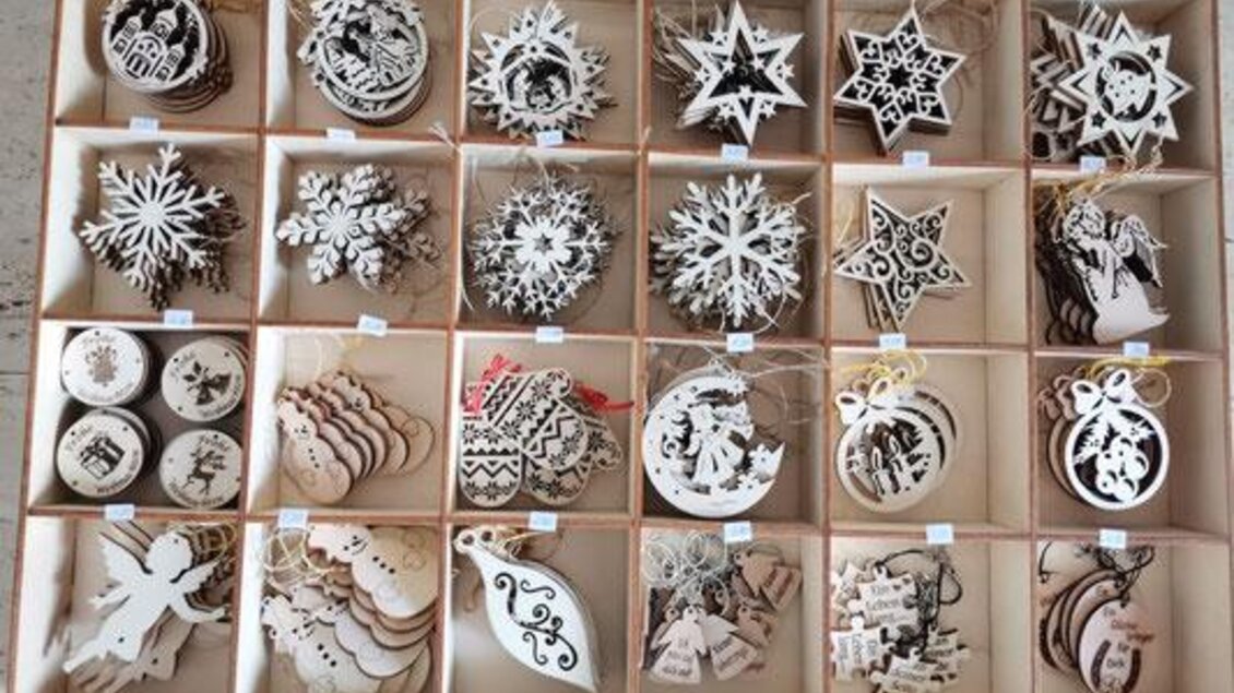 Eine Vielzahl von Holzornamenten ist in kleinen Fächern angeordnet. Die Motive umfassen Sterne, Schneeflocken und Weihnachtsfiguren. | © KM Lasergravuren
