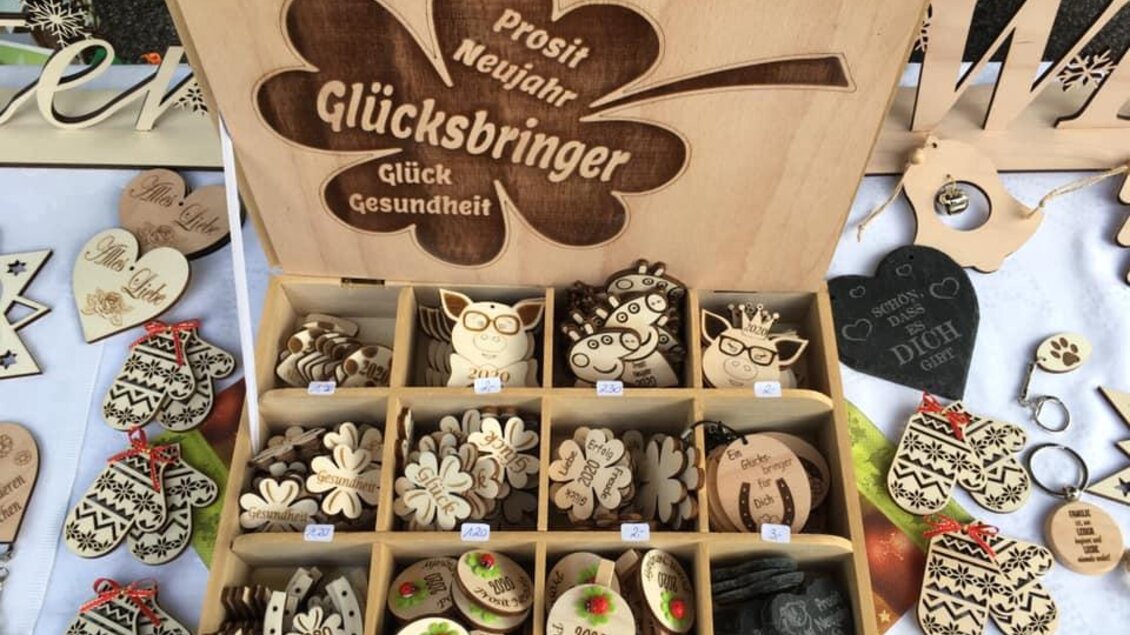 Ein Holzkasten mit verschiedenen Glücksbringern für das neue Jahr. Die Produkte sind liebevoll gestaltet und umfassen Glücksbringer in Form von Kleeblättern und anderen Symbolen. | © KM Lasergravuren