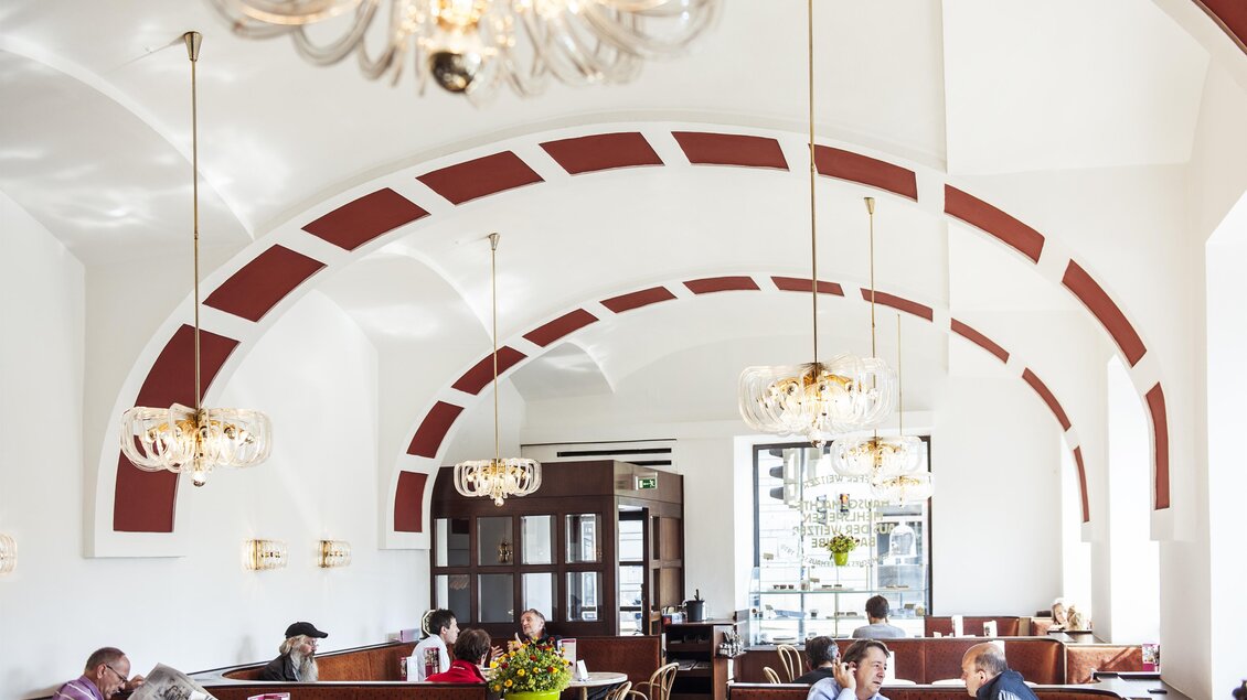 Ein modernes Café mit stilvollem Interieur und gemütlicher Atmosphäre. Menschen sitzen in kleinen Gruppen, während sie essen und sich unterhalten. | © Weitzer