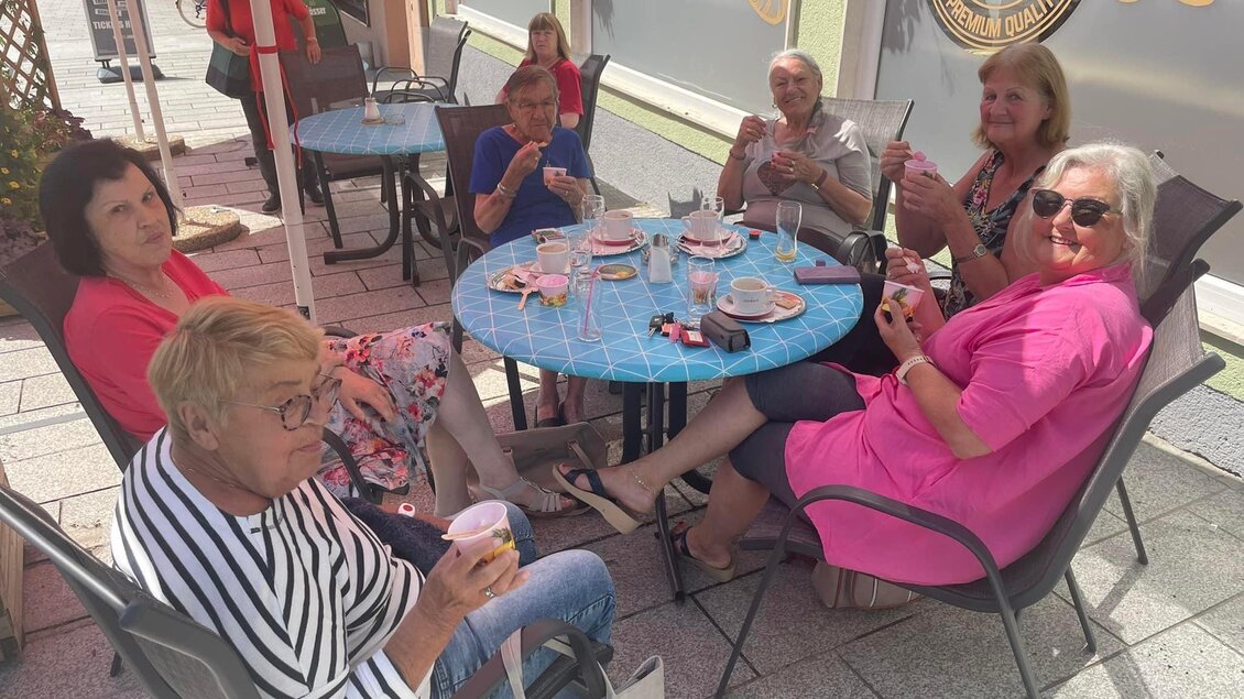 Eine Gruppe von sechs Frauen sitzt an einem Tisch im Freien. Sie genießen Getränke und Snacks in einem gemütlichen Café. | © Peer Dieter
