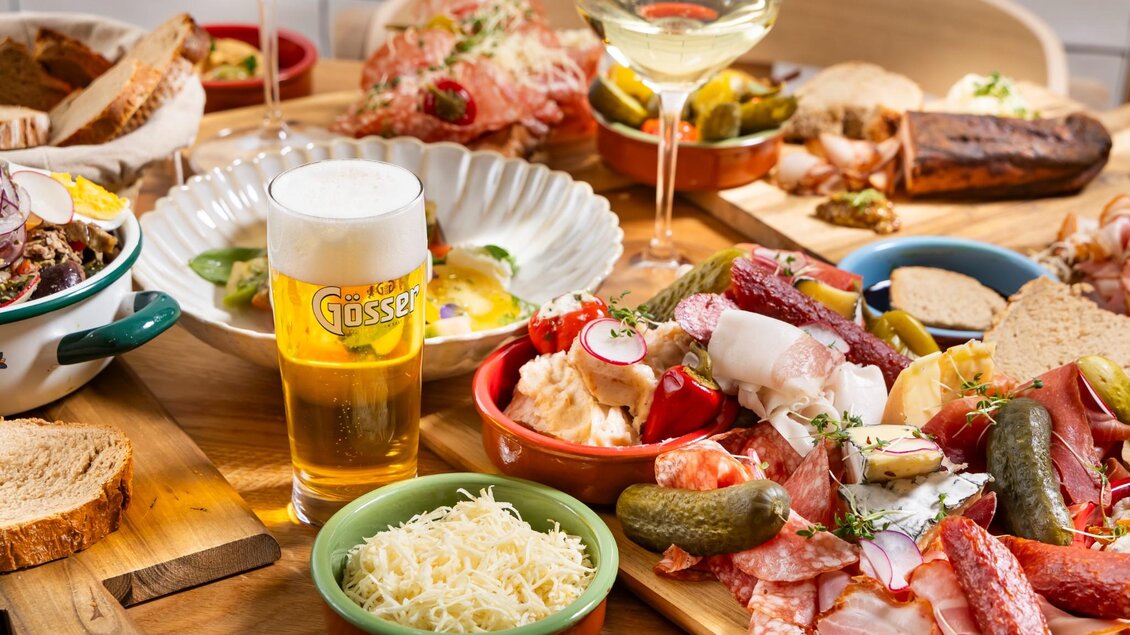 Reich gedeckter Holztisch mit Aufschnitt, Käse, Kren, Brot, eingelegtem Gemüse sowie Bier- und Weingläsern | © Kaiser Greißler - Werner Krug