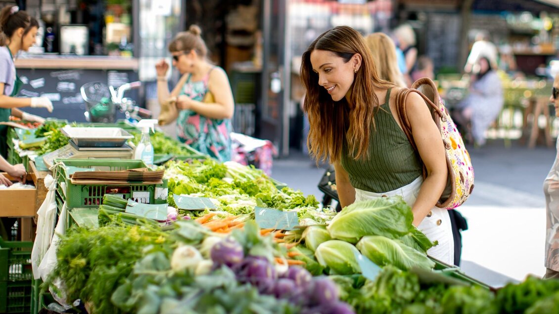 Frau betrachtet frisches Gemüse wie Kohl, Karotten und Salate an einem Marktstand | © Graz Tourismus - Tom Lamm
