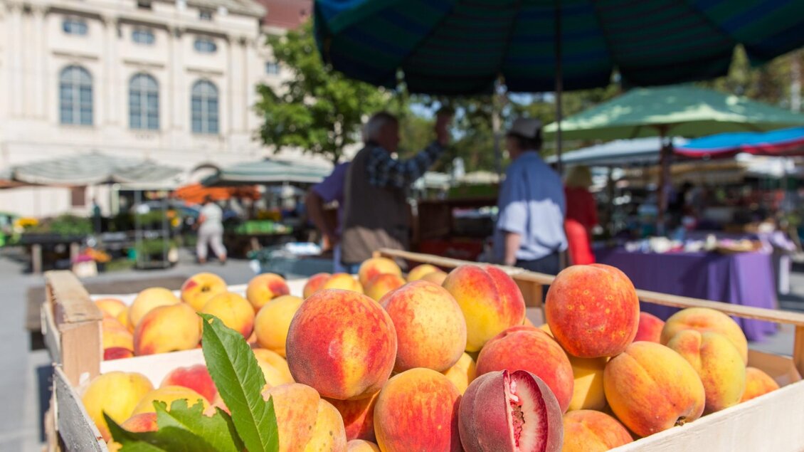 Frische Pfirsiche in Holzkiste auf dem Kaiser-Josef-Markt in Graz, im Hintergrund Marktstände | © Graz Tourismus - Harry Schiffer