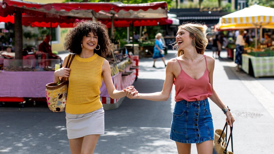 Zwei Frauen laufen lachend nebeneinander über den Markt, eine trägt einen Korb mit Gemüse | © Graz Tourismus - Tom Lamm